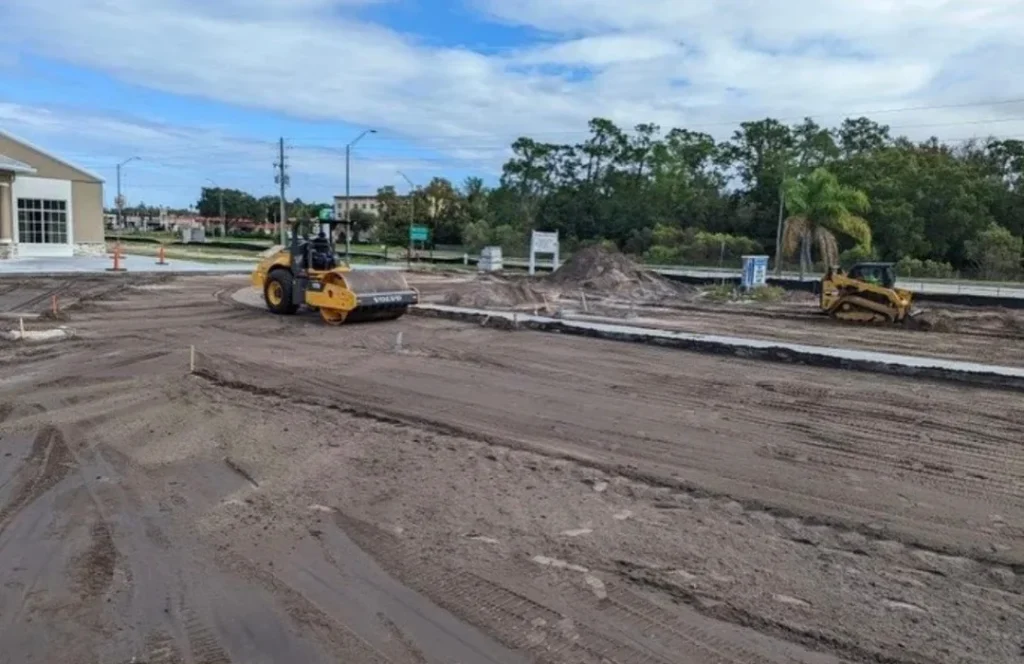 A compact vibratory roller performs crucial subgrade compaction as part of a detailed commercial site development project, preparing a new lot for pavement and curbing.